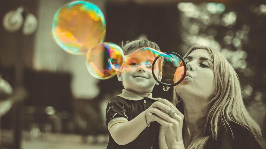 A young woman is blowing bubbles with a toddler and the photo is in black and white apart from the bubbles that are in colour