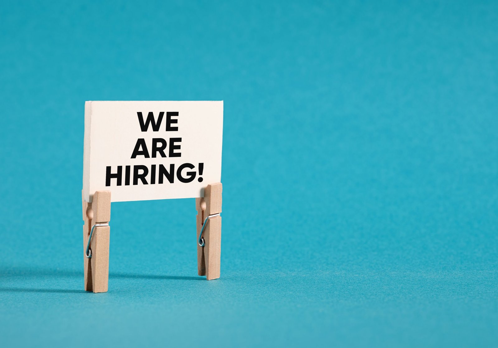 A sign reading 'We are hiring!' is being helo up by two wooden pegs and the images feature a blue background